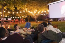 Friends relaxing, watching movie on projection screen in backyard — Stock Photo
