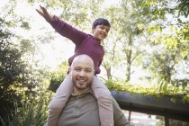 Portrait playful father carrying son on shoulders in park — Stock Photo