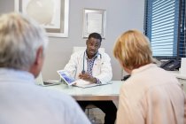 Doctor with digital tablet talking to senior couple in clinic doctors office — Stock Photo