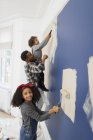 Portrait cute girl painting wall with father and brother — Stock Photo