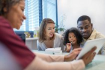 Médico con tableta digital hablando con su familia en el consultorio médico - foto de stock