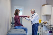 Мужской врач осматривает руку пациентки в комнате обследования клиники — стоковое фото