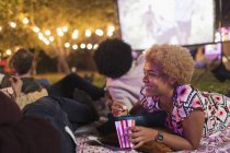 Счастливая женщина ест попкорн, смотрит кино с друзьями на заднем дворе — стоковое фото