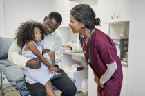 Female pediatrician talking to father and daughter in clinic examination room — Stock Photo