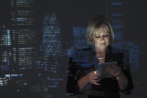 Femme d'affaires double exposition utilisant une tablette numérique avec paysage urbain du soir en arrière-plan — Photo de stock