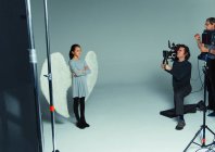 Девушка в ангельских крыльях позирует фотографам во время фотосессии в студии — стоковое фото