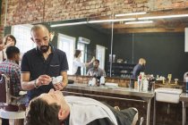 Peluquero masculino que se prepara para afeitar la cara del cliente en la barbería - foto de stock