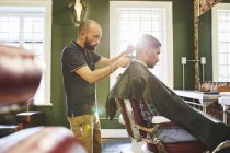 Focado barbeiro masculino dando ao cliente um corte de cabelo na barbearia — Fotografia de Stock