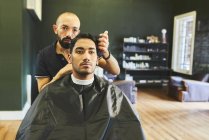 Barbeiro masculino dando corte de cabelo ao cliente na barbearia — Fotografia de Stock