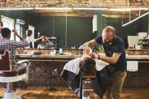 Barbeiro masculino barbeando rosto de cliente na barbearia — Fotografia de Stock
