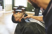 Barbeiro masculino escovando rosto de cliente na barbearia — Fotografia de Stock