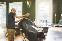 Barbeiro masculino dando ao cliente um corte de cabelo na barbearia — Fotografia de Stock