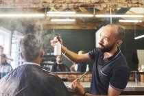 Peluquería masculina rociando el cabello del cliente en la barbería - foto de stock