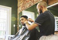 Peluquería masculina dando al cliente un corte de pelo en la barbería - foto de stock