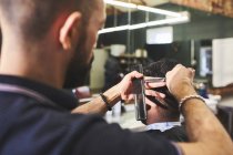 Maschio barbiere dando al cliente un taglio di capelli in barbiere — Foto stock