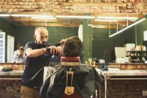 Barbeiro masculino dando ao cliente um corte de cabelo na barbearia — Fotografia de Stock