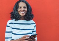Portrait of smiling, confident woman using smartphone against red background — Stock Photo