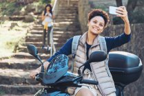 Young woman taking selfie with camera phone on motor scooter — Stock Photo