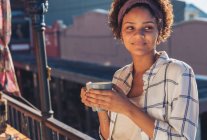 Усміхнена молода жінка п'є каву на сонячному балконі — стокове фото
