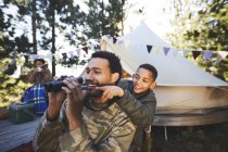 Happy, curious father and son with binoculars at campsite — Stock Photo