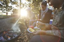 Family eating at sunny campsite campfire in woods — Stock Photo