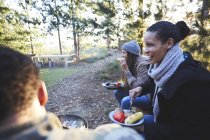 Happy friends eating at campsite in woods — Stock Photo