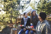 Happy friends laughing and eating at campsite in woods — Stock Photo