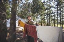 Retrato del hombre feliz colgando la ropa en el tendedero del camping en los bosques - foto de stock