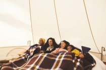 Happy lesbian couple and kids relaxing under blanket in bed in camping yurt — Stock Photo