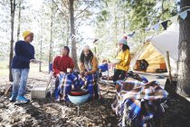 Coppia lesbica e bambini che cucinano alla griglia del campeggio nei boschi soleggiati — Foto stock