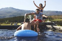 Игривая семья плавает в солнечном летнем бассейне — стоковое фото