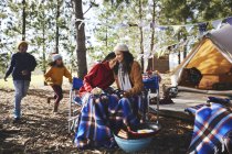 Feliz, casal lésbico afetuoso com crianças relaxando no acampamento na floresta — Fotografia de Stock