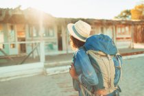 Young female backpacker approaching sunny beach hut — Stock Photo