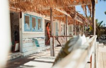 Frau im Bikini steht vor Tür einer sonnigen Strandhütte — Stockfoto