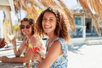 Portrait happy women drinking cocktails at sunny beach bar — Stock Photo