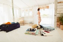 Женщина, стоящая в пляжной хижине, за дверью чемодана и вещей на кровати — стоковое фото