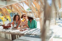 Счастливые женщины пьют коктейли в солнечном пляжном баре — стоковое фото