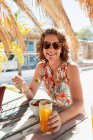 Retrato mujer feliz comiendo y bebiendo en el soleado bar de la playa - foto de stock