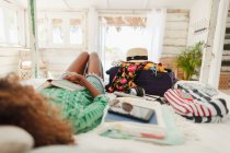 Молода жінка з книгою розслабляється на ліжку поруч з валізою і речами в спальні пляжної хатини — стокове фото