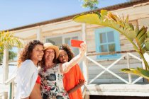 Happy mother and adult daughters taking selfie outside sunny beach hut — Stock Photo