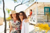 Portrait happy mother and adult daughter outside sunny beach hut — Stock Photo