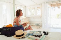 Serena mulher escrevendo em diário ao lado de mala em cabana de praia quarto — Fotografia de Stock