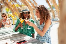 Счастливые молодые женщины-друзья пьют коктейли в солнечном пляжном баре — стоковое фото