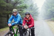 Retrato padre e hijo ciclismo de montaña bajo la lluvia - foto de stock