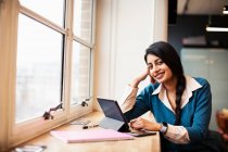 Портрет уверенный, улыбающаяся деловая женщина с помощью цифрового планшета в окне — стоковое фото