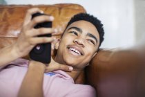 Улыбающийся подросток с помощью смартфона на диване — стоковое фото