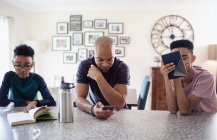 Батько і сини використовують цифровий планшет, смартфон і книгу для читання на кухні — стокове фото