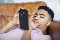 Мальчик-подросток с помощью смартфона на диване — стоковое фото