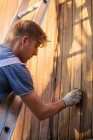 Maschio lavoratore su scala colorazione legno raccordo su esterno casa — Foto stock