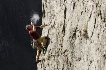 Männlicher Bergsteiger erklettert Felswand, blickt auf und bläst Kreide auf die Hände — Stockfoto